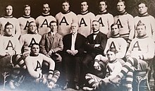 Black and white team photo, with fourteen men dressed in football uniforms and two men dressed in suits