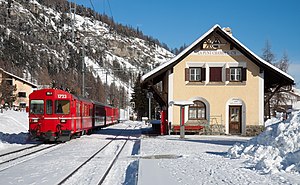 Two-story building with gabled roof in the snow and a red train adjacent