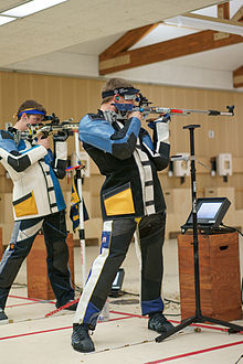 Photograph of two men, standing, in shooting jackets, firing rifles.