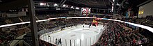 A panoramic view of a hockey rink with a large inflatable dragon head on the ice