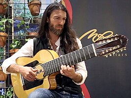 seated Estas Tonne playing an acoustic 10-string guitar