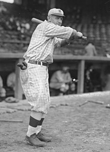 A man in an old-fashioned baseball uniform holds his bat above his shoulder, left-handed