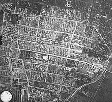 An aerial photograph of the former Warsaw Ghetto area, showing the camp's structure (a long and narrow rectangle in the image's centre) surrounded by Warsaw Ghetto's ruins