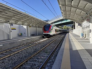 White-and-red train on tracks next to side platform and passing under overpass