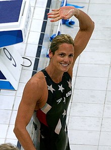 Color photo of smiling Torres in navy blue bathing suit with white stars, waving to crowd.