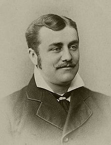 A man with sideburns and a mustache wearing a shirt with his collar sticking out over his jacket