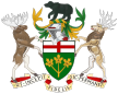A central shield with the upper part showing the red cross of St. George and the lower part showing three golden maple leaves on a green background. There is a black bear on top of a knight's helmet above the shield with a moose to the left and a Canadian deer to the right. The province's motto "Ut incepit Fidelis sic permanent", Latin for "Loyal she began, loyal she remains" is written below the crest.