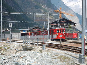 Red-and-white train in front of four-story chalet-style building with gabled roof