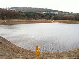 A reservoir at low volume showing stones on the surrounds, with trees in the distance