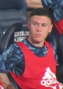 Patricio Nehuén Pérez wearing a red Adidas training bib while sat in the dugout of a football stadium