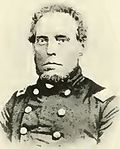 Sepia toned rendering of a square-faced man with a short beard and a receding hairline. He wears a dark military uniform.