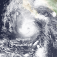 A satellite image of a hurricane with a ragged and cloudy eye just southwest of the southern tip of the Baja California peninsula