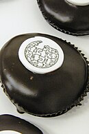 A chocolate covered cupcake topped with the Wikipedia logo stenciled on a white chip