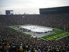 A hockey rink is set up in the middle of a football field, with thousands of people surrounding the playing surface