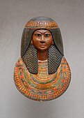 Mummy mask wearing large wig and floral collar