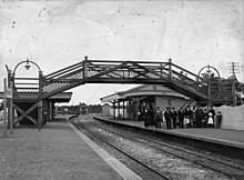 Black and white image of a railway station with two side platforms and a footbridge