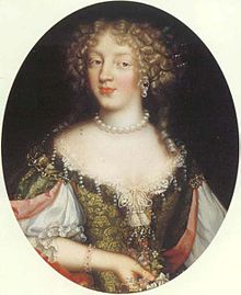 Half-length oil portrait painting in an oval format of a grey-eyed young woman with fair curly hair wearing a pearl necklace and clad in a low-necked dress with a split bodice in stiff brocade bound with a pearl rope