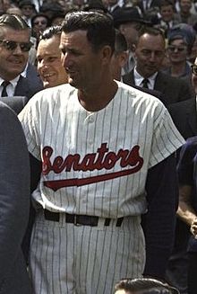A man in a white baseball uniform with "Senators" on the chest in red