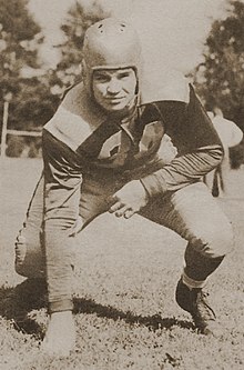 Black and white photo of Adams in a football stance with his uniform on