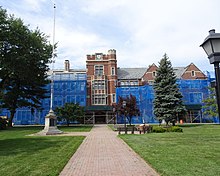 A stone building with central tower. Much of the facade is covered in blue tarps