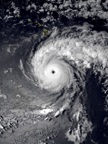 A satellite image of a powerful hurricane south of the Big Island of Hawaii. It has a clear and well-defined eye surrounded by a circular area of intense convection; a pronounced outer band originates from the western side of the storm and curves clockwise a quarter of the way around it, before jutting out to the east.