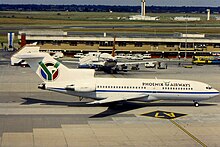 A profile view of a white, mid-sized commercial airliner sits on the tarmac at an airport. It has the words Phoenix Airways painted on the side near the front along with a logo on its tail that pays homage to the South African flag.