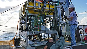 Two men are preparing a remotely operated vehicle for an underwater expedition.