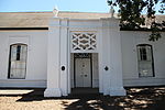 Just a short distance higher up from La Gratitude on the left side of Dorp Street, stands a modest little building with a peculiar verandah. It looks rather out of place among the rest of the buildings by which it is squeezed in. This is the Stellenbosch Gymnasium from which the Paul Roos Gymnasium and the University of Stellenbosch developed.