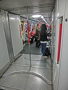 Interior of refurbished Metro-Cammell M-Train EMU. Visible changes include the red grab poles, new seats, new longitudinal instead of transverse lighting, overhead system maps with LED indicators, and new red handles replacing the black bell-shaped strap hangers.