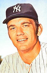 A man in a white baseball uniform with navy pinstripes and a navy cap