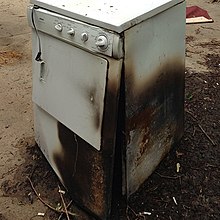A white clothes dryer with charred sides sitting outdoors on pavement