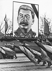 A man with dark hair and moustache, wearing a uniform, posted over a military parade