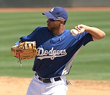A man in a blue baseball jersey with "DODGERS" on the chest with a baseball glove on his right hand prepares to throw a baseball with his left hand.