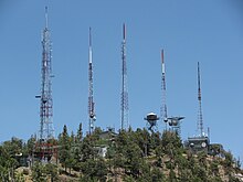 A mountaintop with five towers with multiple broadcasting and communications antennas attached.
