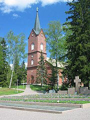 Traditional four-square brick church. In the foreground, attached to the church, is a three-storey brick steeple with Romanesque windows and a weathered copper spire is set on grassy area amid trees.
