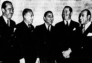 Black-and-white newspaper photograph of five suited men smiling jubilantly; the middle man eyes the camera. The man at the far left has a toothbrush mustache. On the wall behind them, a vision of faded backwards writing bleeds through from another page of the paper.