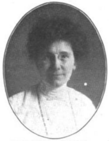 A photograph of a white woman in an oval frame; she is wearing eyeglasses and a white blouse with a high collar