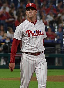 A baseball player in a white uniform with red vertical pinstripes