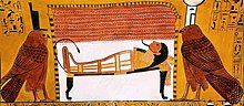 Large birds flanking a mummy lying on a bed inside a tent
