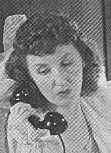 A white woman with a curled hairstyle, holding a telephone