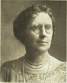 B&W portrait photo of a middle-aged woman wearing glasses, pearls, and a beaded blouse.