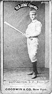 A baseball player is standing, facing the camera, holding a baseball bat.