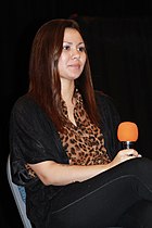 A women is seated at a chair and holding a microphone