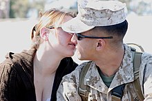 A white man in digital camouflage kisses a white woman in civilian clothes.