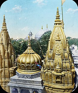 The Kashi Vishwanath Temple was destroyed by the army of Qutb ud-Din Aibak in 1194 CE. Since then, it has been demolished twice (in the 1400s, and 1669 CE) and rebuilt four times (in the 1200s, twice in the 1500s under Akbar, and in the 1800s). Shown is the current 1800s temple, with the white domes and minaret of the co-located 1600s Gyanvapi Mosque in the background. The tonne of gold for the temple roof was donated by Ranjit Singh in 1835.[135][136]