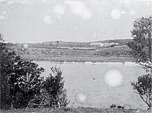 A black and white photo of a lake with a house in the distance.