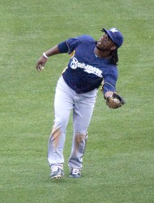 A man wearing a navy blue Brewers jersey and cap with gray pants after catching a ball on a green field