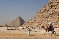Tourists riding a camel in front of Giza pyramids