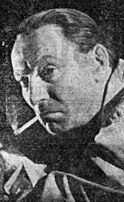 A black-and-white image of a 42-year-old man smoking a cigarette and looking to the left of the camera.