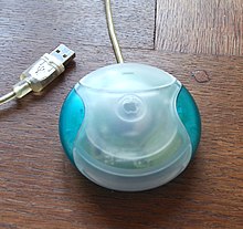 Overhead view of a round, translucent plastic peripheral on a wooden desk. Circuitry inside is partially visible beneath the blue-and-white plastic.
